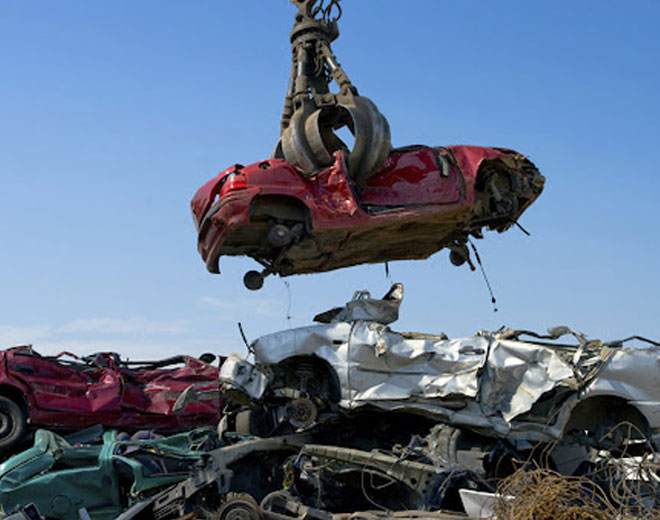 A crane lifts a car from a heap of scrap, illustrating the process of recycling and salvage operations.